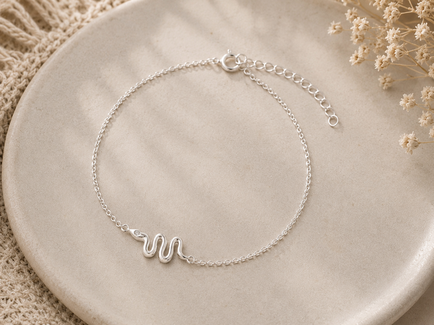 "Snake Chain Bracelet Sterling Silver product shot — delicate silver cable chain bracelet with polished serpentine snake charm centred, spring ring clasp and extender chain, on cream ceramic dish with dried gypsophila"
