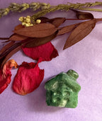 Moss Agate crystal house carving front view on purple background with red rose petals — The Crooked Moon