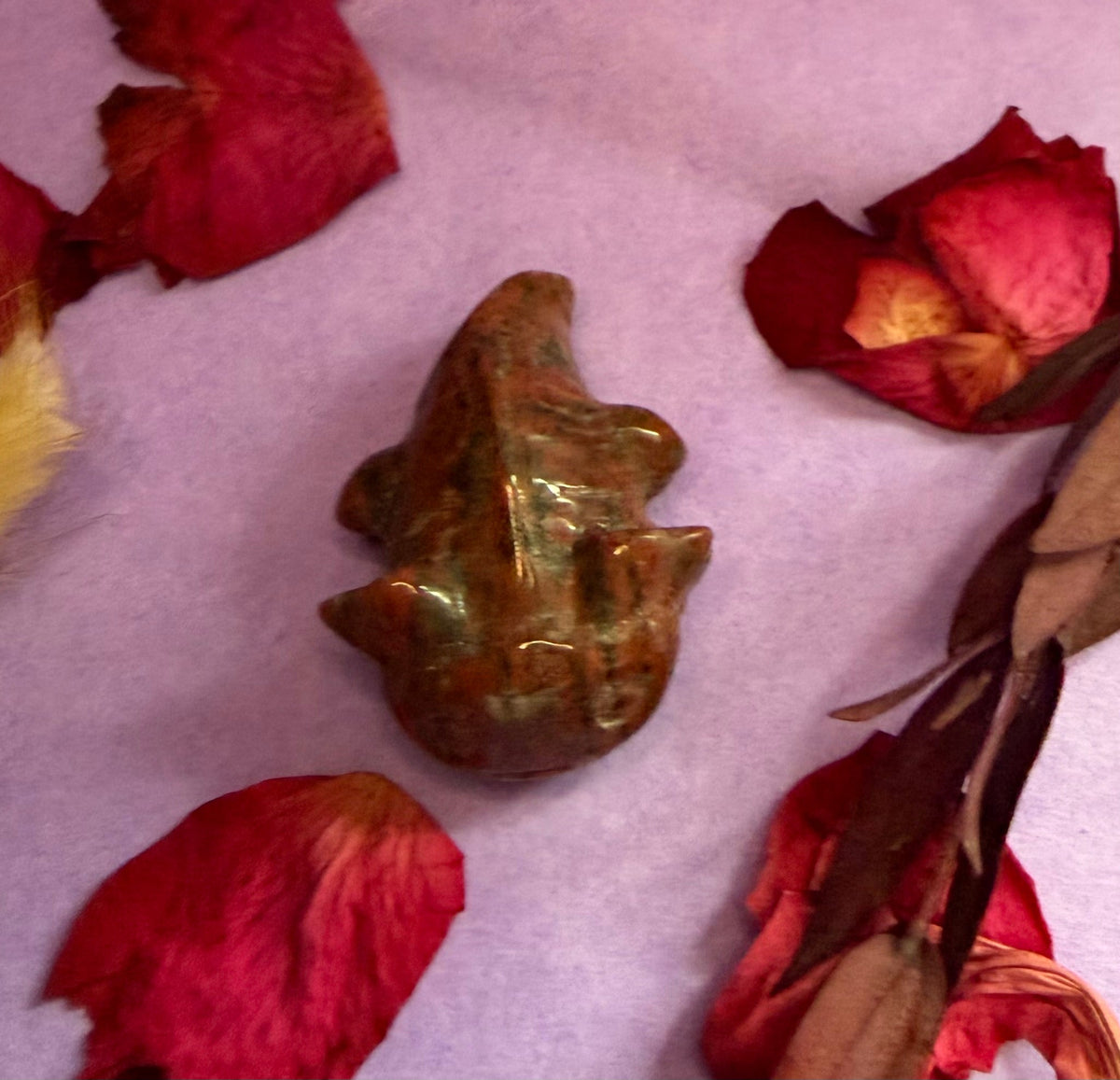 Mahogany Obsidian crystal axolotl carving side view on purple background with rose petals — The Crooked Moon