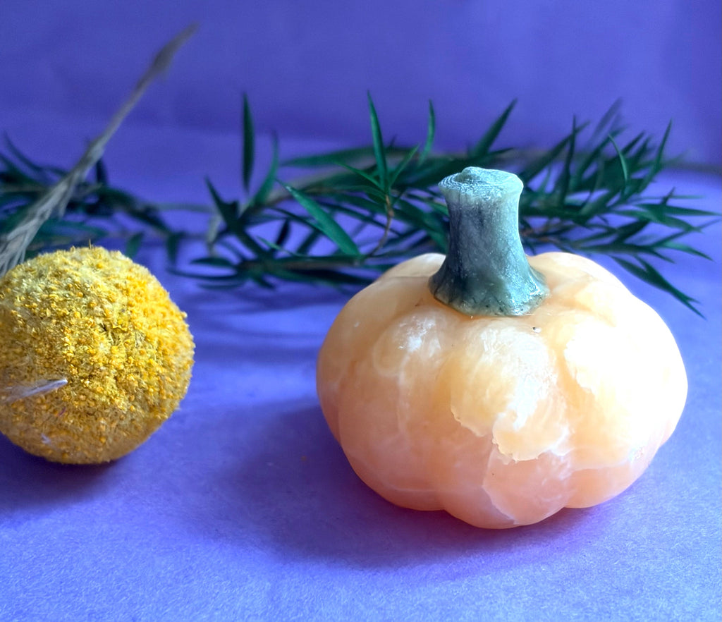 Orange Calcite crystal pumpkin carving with Green Aventurine stem on lilac background — The Crooked Moon