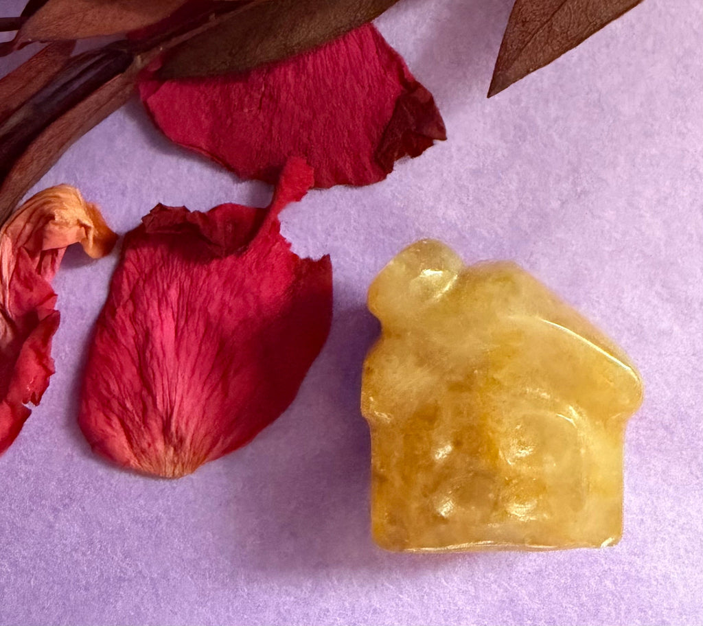 Golden Healer Quartz crystal house carving front view on purple background with red rose petals — The Crooked Moon