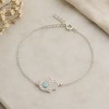 "Hamsa Hand Bracelet Sterling Silver product shot — delicate silver chain bracelet with pavé CZ hamsa hand charm and turquoise centre stone, spring ring clasp and extender chain, on cream marble surface with dried gypsophila"