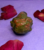 Unakite crystal frog carving front view on purple background with rose petals — The Crooked Moon