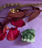 Moss Agate crystal house carving side view on purple background with red rose petals — The Crooked Moon
