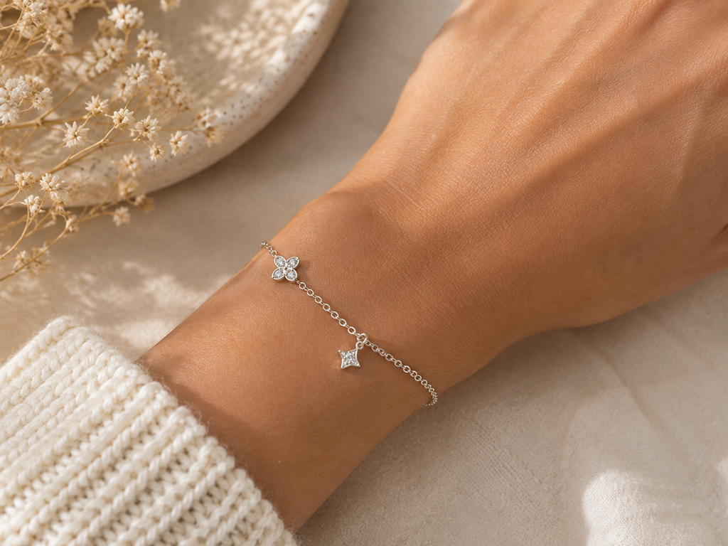 "Dual Star CZ Bracelet Sterling Silver worn shot — delicate silver chain bracelet with two sparkling pavé CZ star charms shown worn on model's wrist over white knit sleeve, cream dish and dried gypsophila in background"