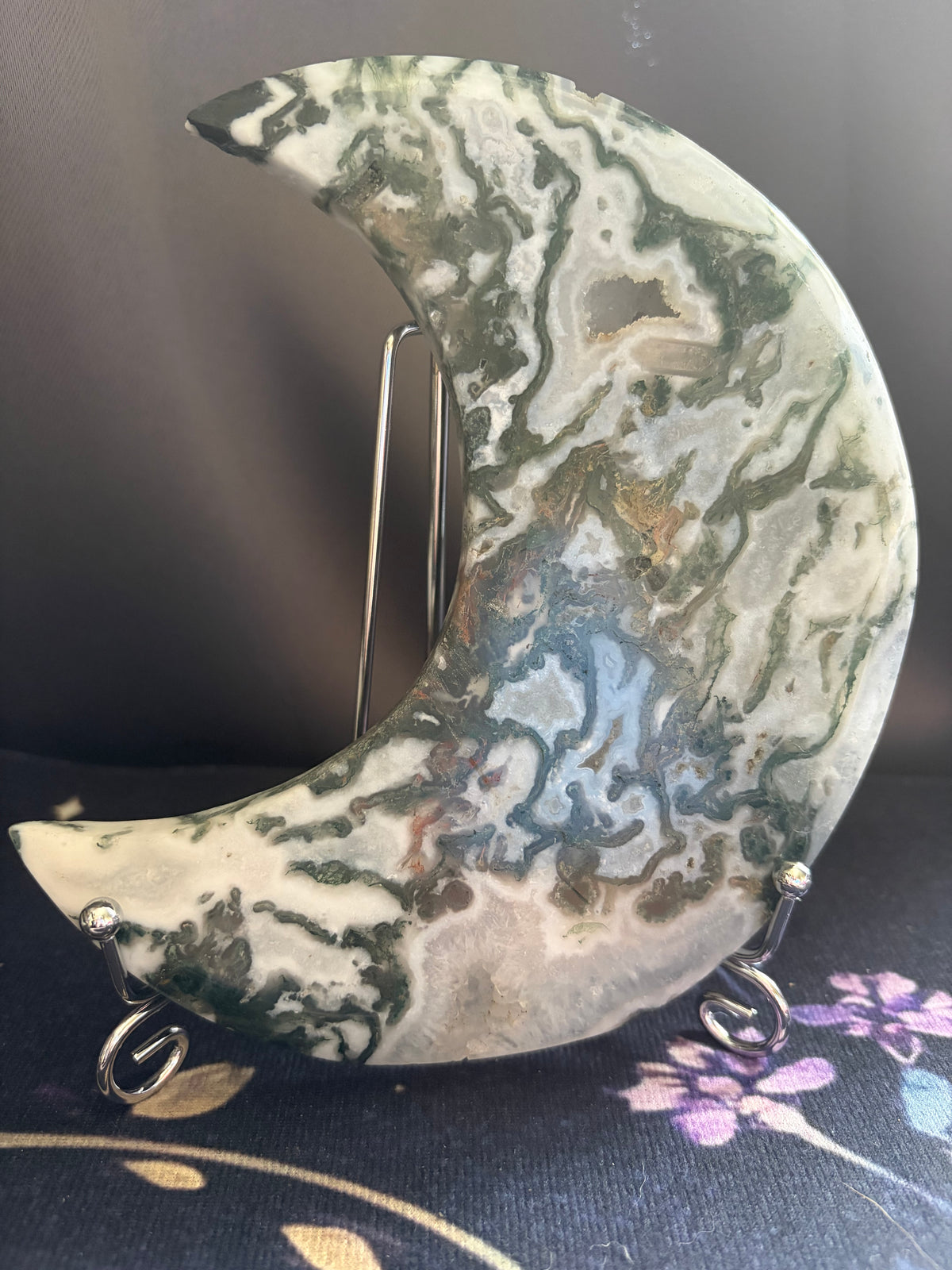 A crescent moon-shaped decorative object made of marbled agate or stone, displayed on a small metal stand against a dark background.