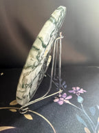 A polished green and white marbled stone plaque or coaster displayed on a small metal stand against a dark background.