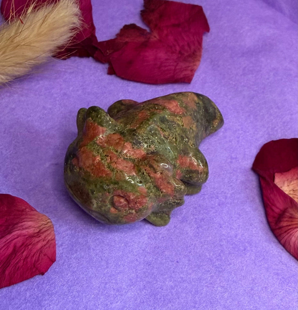 Unakite crystal frog carving side view on purple background with rose petals — The Crooked Moon