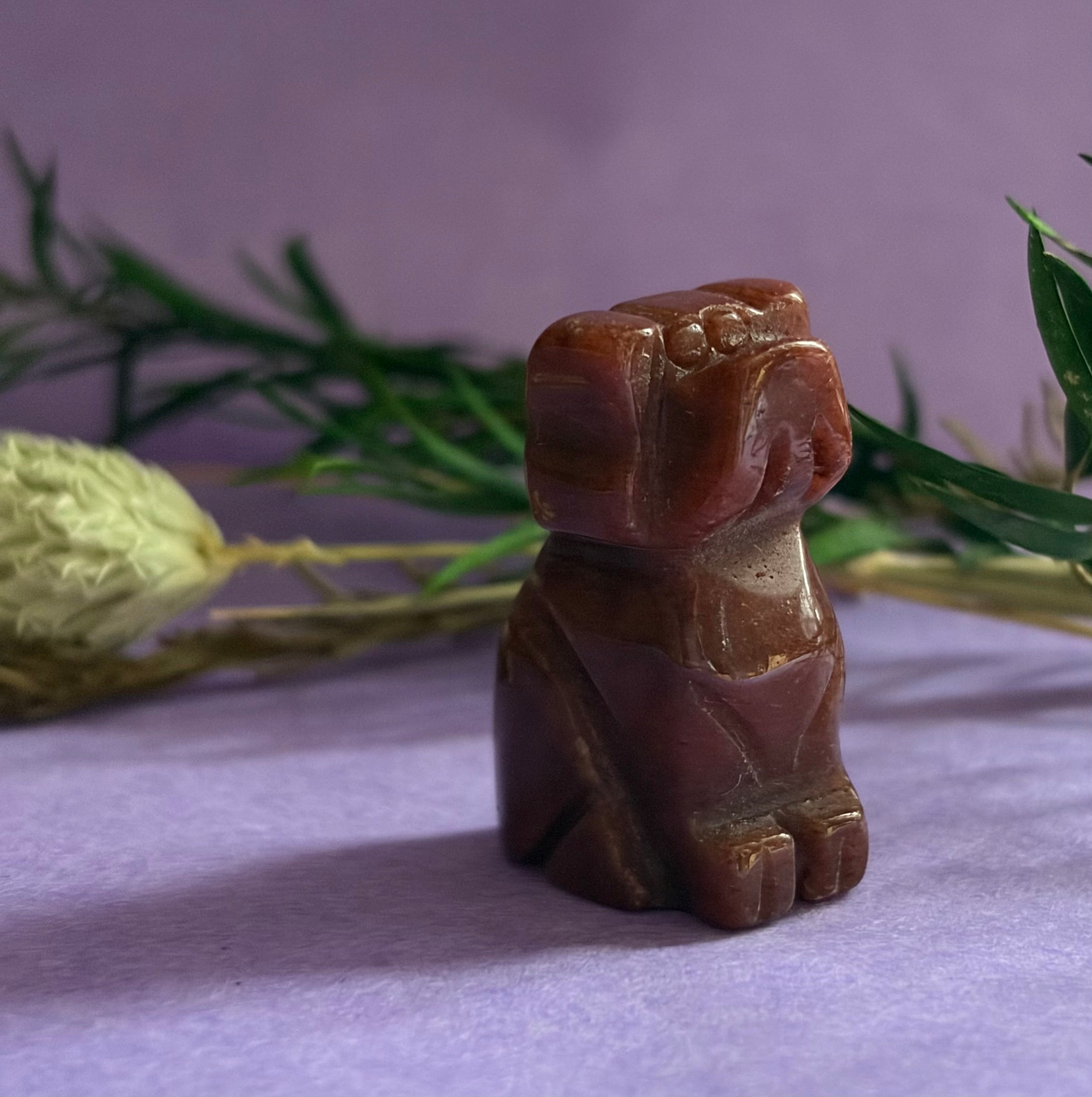 Red Goldstone crystal dog carving on lilac background with green foliage — The Crooked Moon