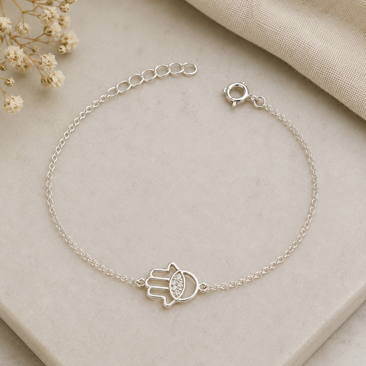 "Open Hamsa Evil Eye Bracelet Sterling Silver product shot — delicate silver chain bracelet with open cutout hamsa hand charm and pavé CZ evil eye, spring ring clasp and extender chain, on cream stone surface with dried gypsophila"