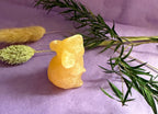 Orange Calcite crystal mouse carving three-quarter view on purple background with dried botanicals — The Crooked Moon