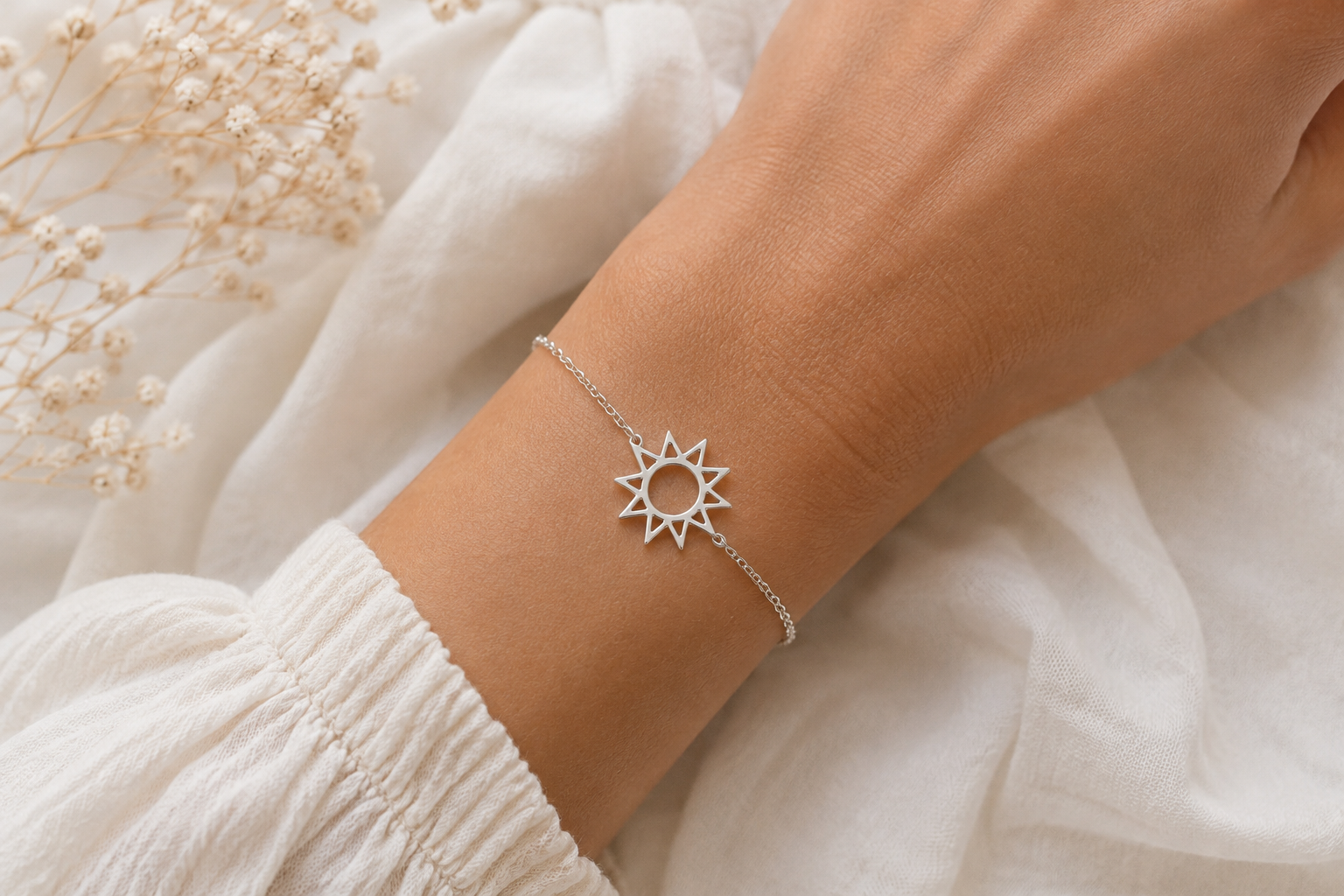 "Sun Charm Chain Bracelet Sterling Silver worn shot — delicate silver chain bracelet with open geometric sun charm shown worn on model's wrist against white linen fabric with dried gypsophila in background"