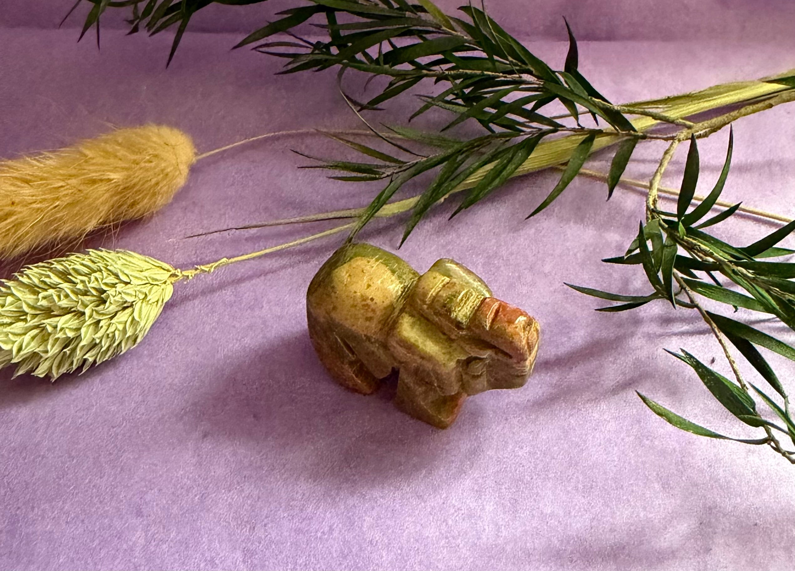 Unakite crystal elephant carving top view on purple background with dried botanicals — The Crooked Moon