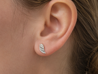 A close-up of a person's ear wearing a small silver wing-shaped stud earring with a clear crystal center.
