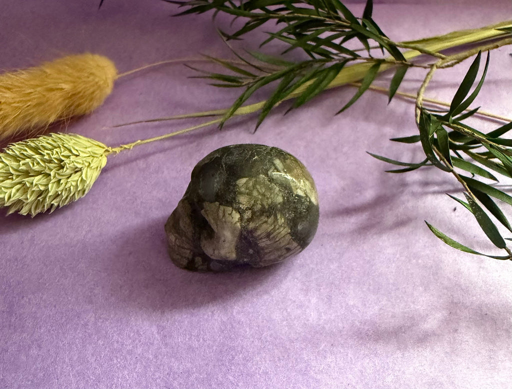 Green Fluorite crystal skull carving angled view on lilac background — The Crooked Moon
