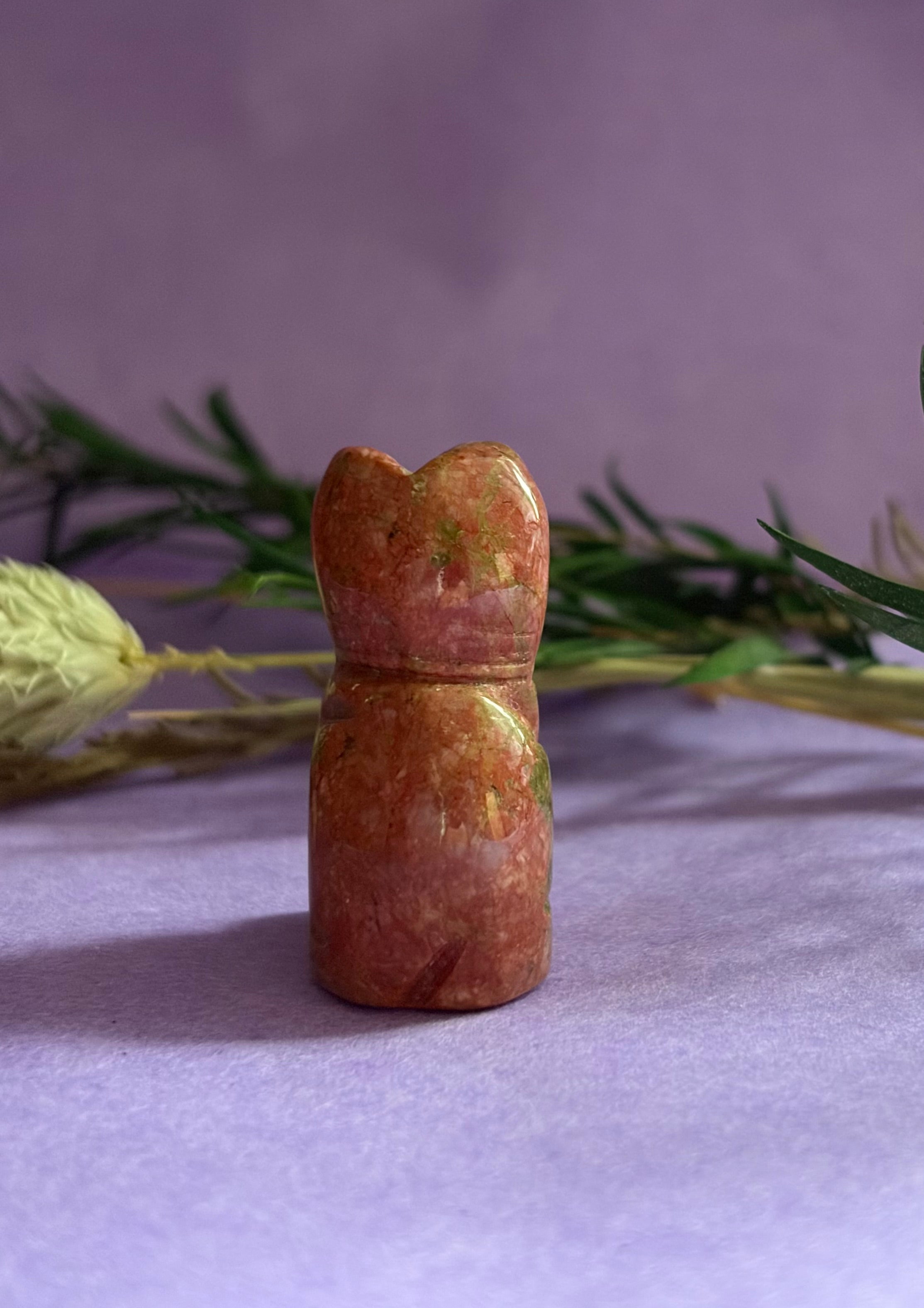 Unakite crystal cat carving back view on lilac background with green leaves — The Crooked Moon