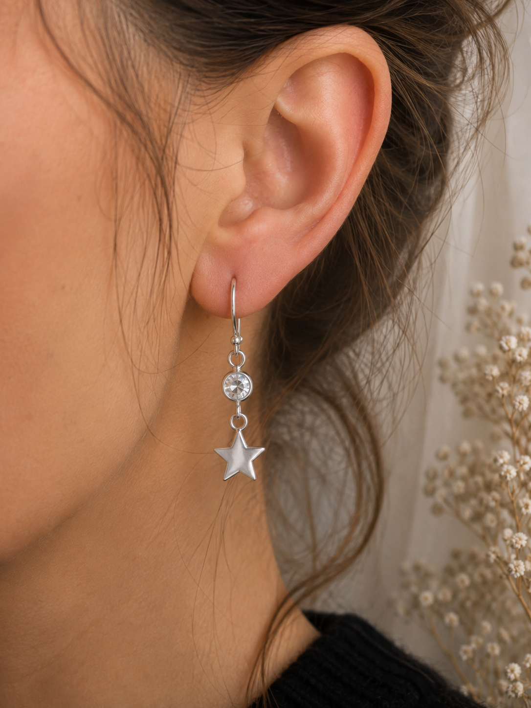 Crystal & Star Drop Earrings Sterling Silver close-up worn shot — single silver hook earring with round bezel-set CZ crystal and polished five-pointed star charm shown worn on model's ear, dried gypsophila in background"