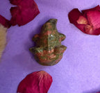 Unakite crystal frog carving top view on purple background with rose petals — The Crooked Moon