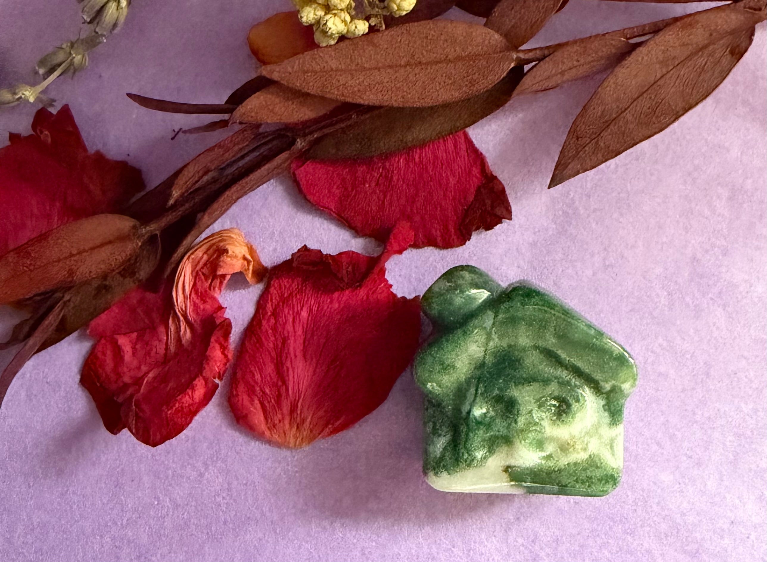 Moss Agate crystal house carving front view on purple background with red rose petals — The Crooked Moon