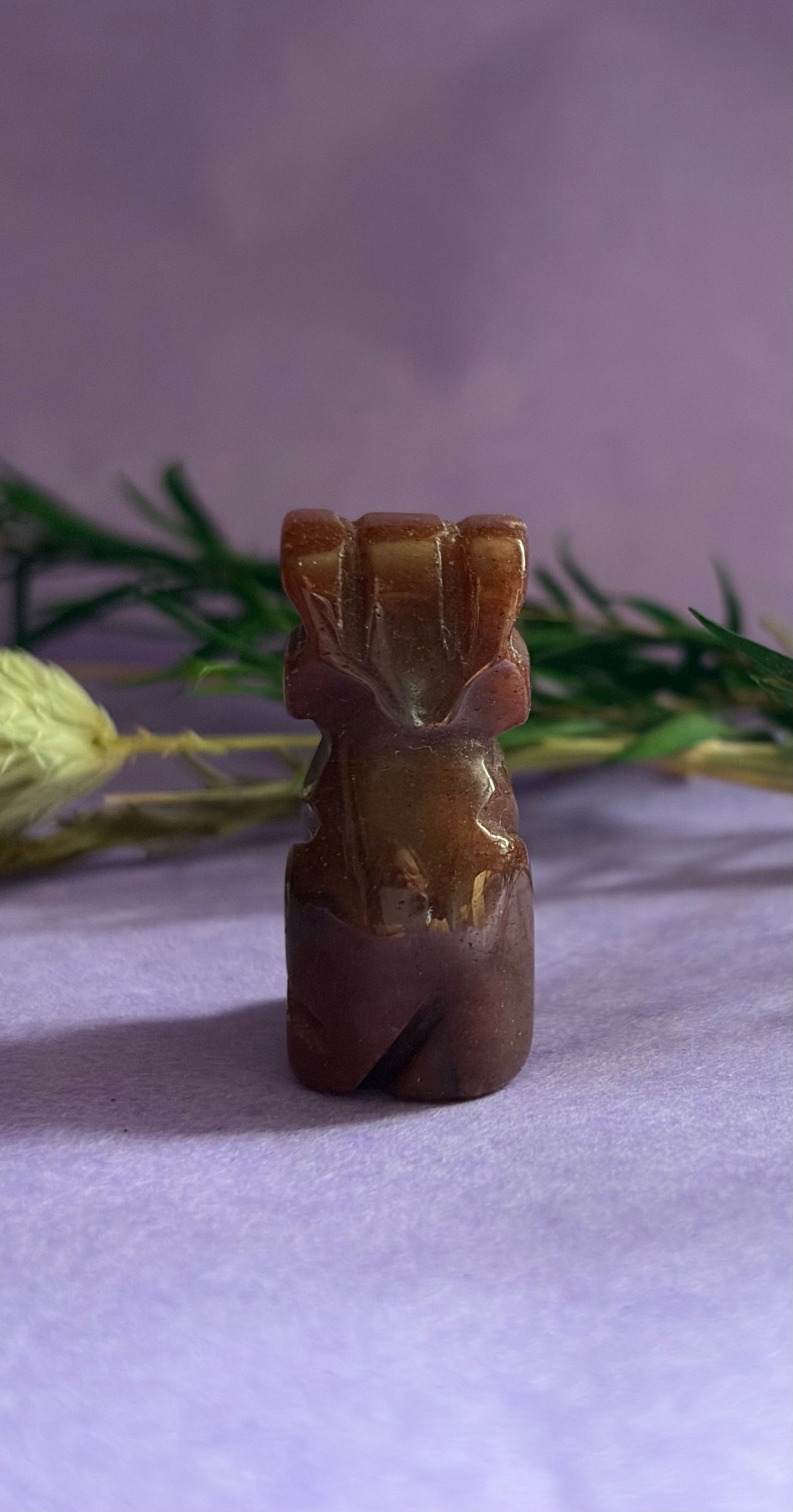 Red Goldstone crystal dog carving back view on lilac background with dried botanicals — The Crooked Moon