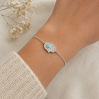 "Hamsa Hand Bracelet Sterling Silver worn shot — delicate silver chain bracelet with pavé CZ hamsa hand charm and turquoise stone shown worn on model's wrist over white knit sleeve, dried gypsophila in background"