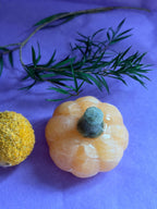 Orange Calcite crystal pumpkin carving top view on lilac background with foliage — The Crooked Moon