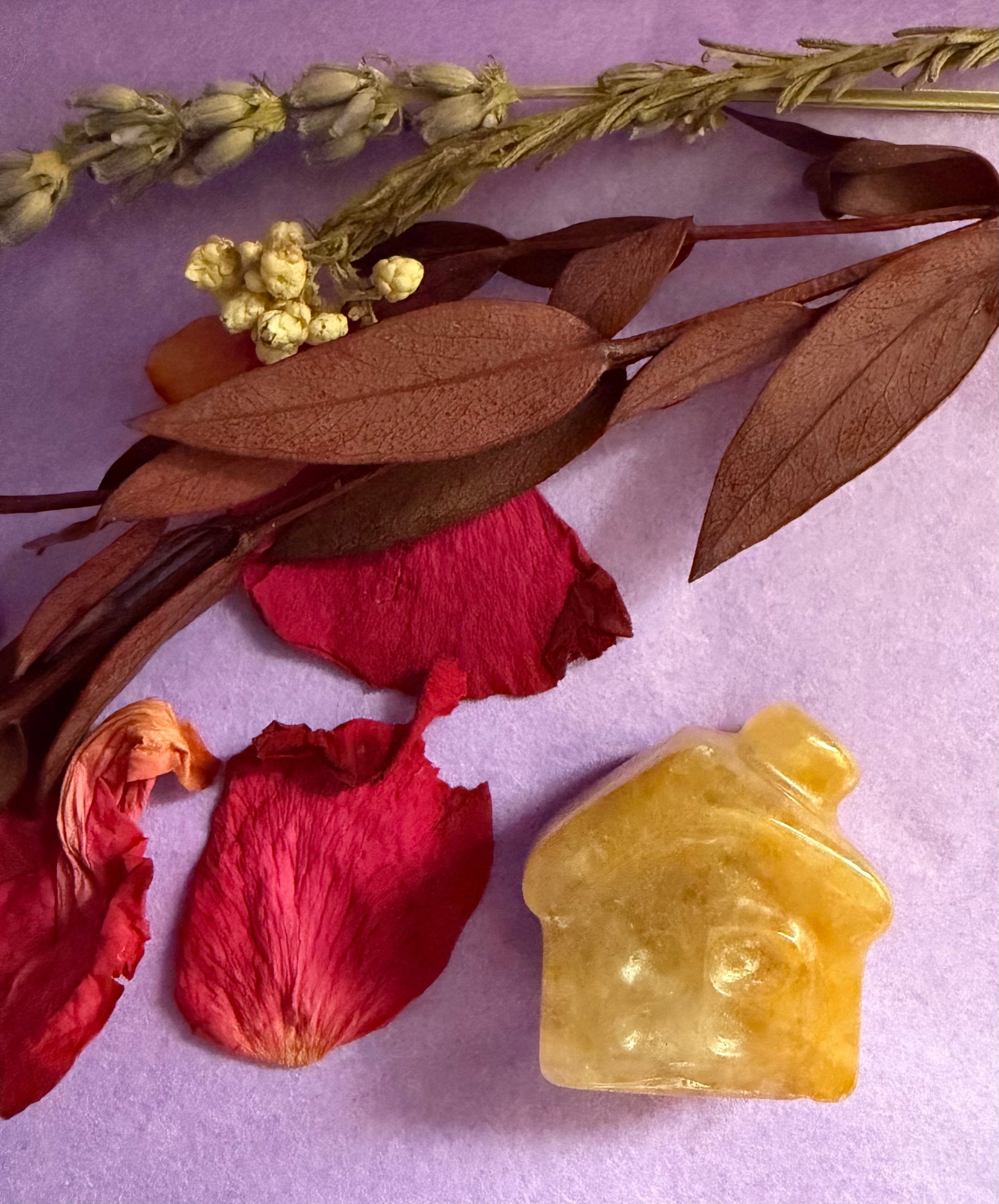 Golden Healer Quartz crystal house carving overhead view on purple background with red rose petals — The Crooked Moon