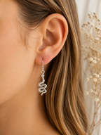 Snake Drop Earrings Sterling Silver worn shot — single silver hook earring with polished coiled snake charm and CZ stone shown worn on model's ear with dried gypsophila in background"
