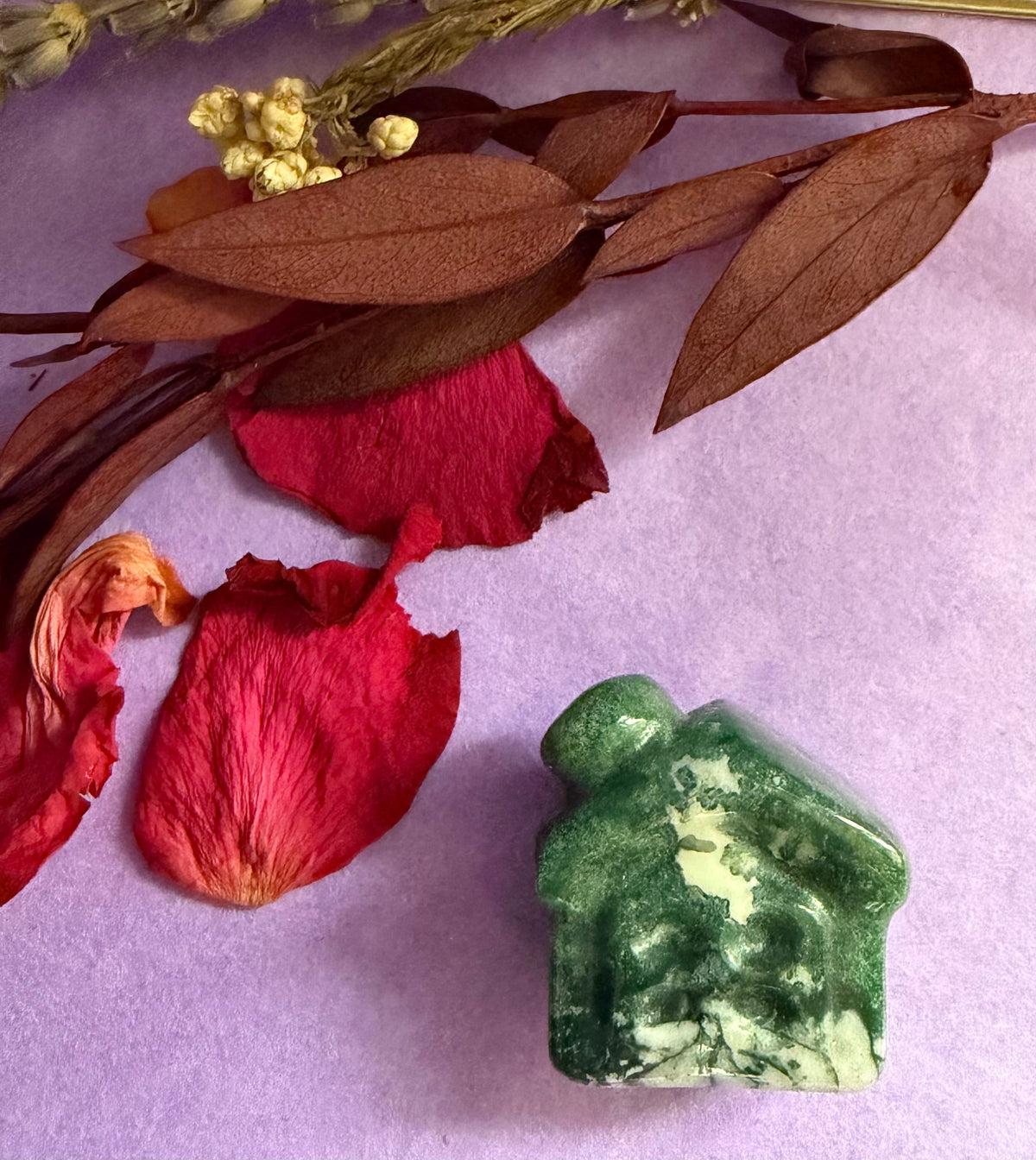 Moss Agate crystal house carving side view on purple background with red rose petals — The Crooked Moon