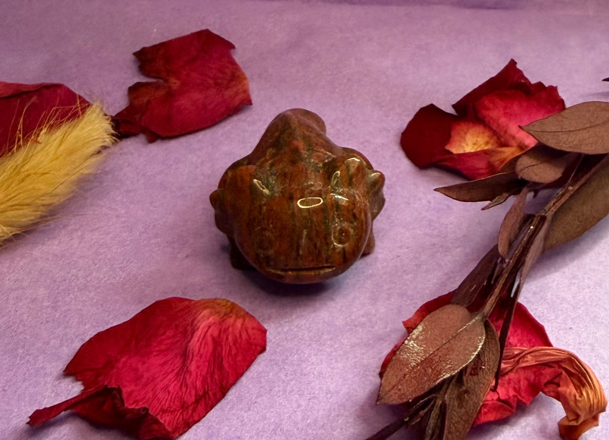 Mahogany Obsidian crystal axolotl carving front view on purple background with rose petals — The Crooked Moon