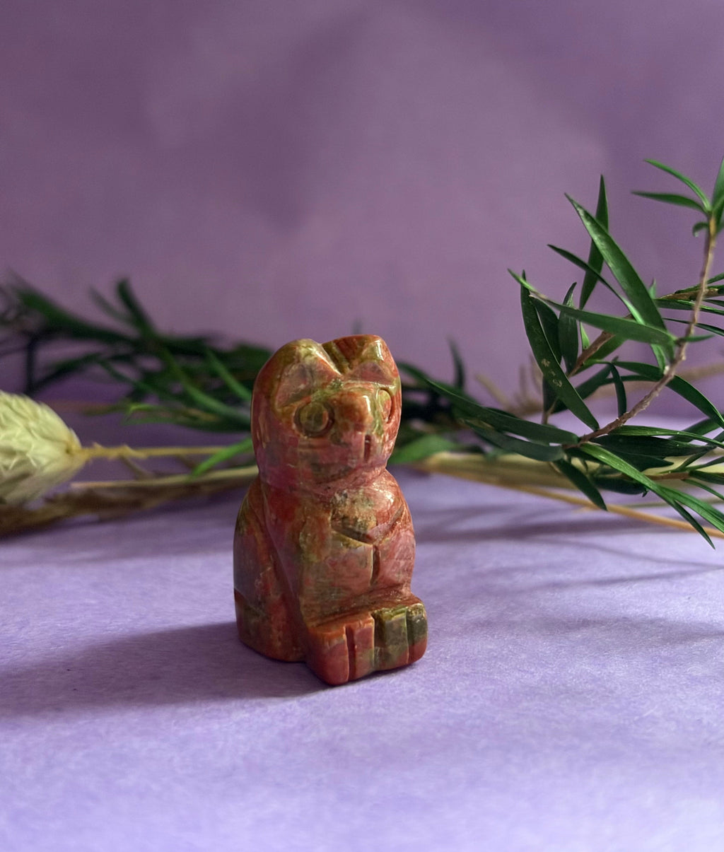 Unakite crystal cat carving on lilac background with green foliage — The Crooked Moon