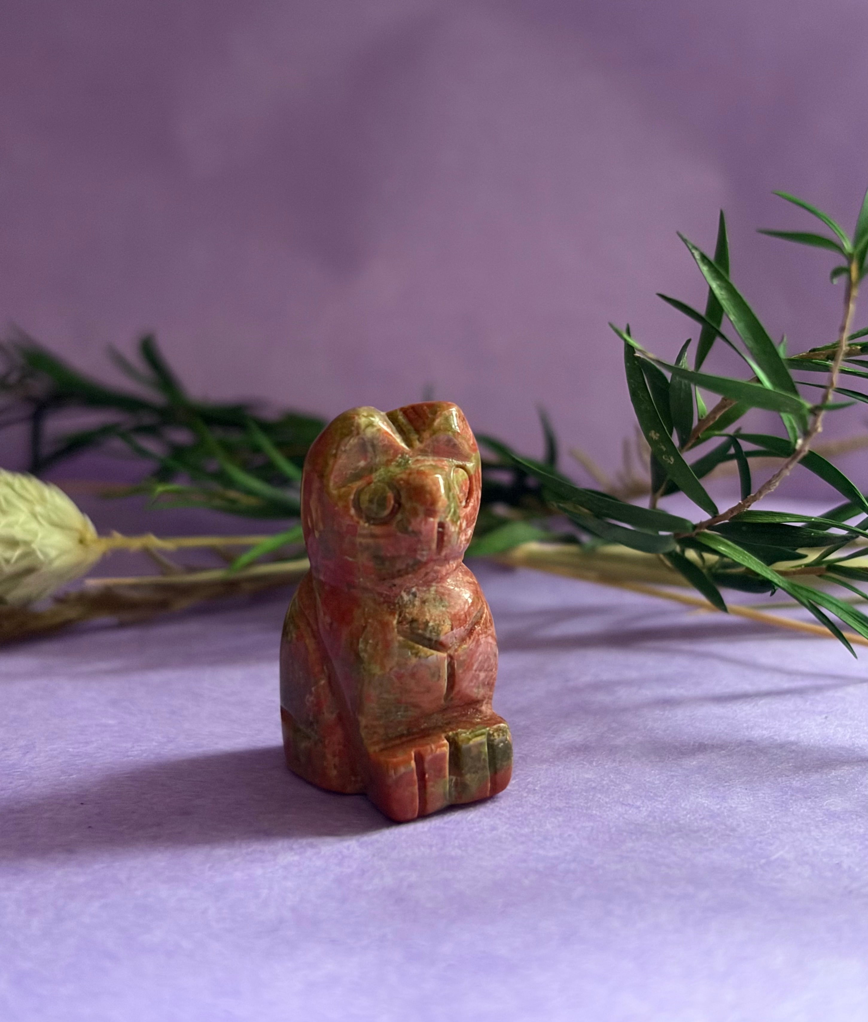 Unakite crystal cat carving on lilac background with green foliage — The Crooked Moon