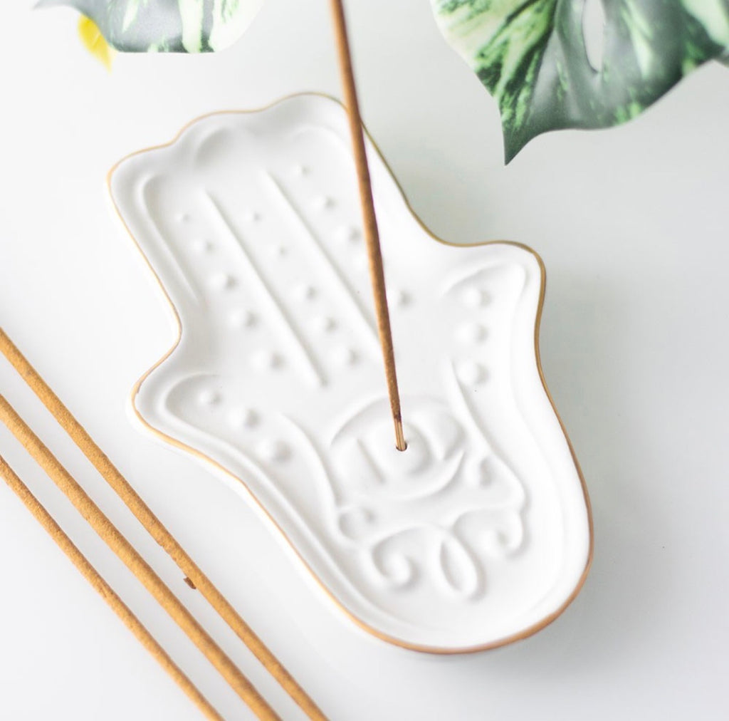 Hamsa Hand Incense Stick Holder lifestyle shot with incense stick burning on white surface with tropical leaves