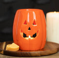 Jack-o'-Lantern Pumpkin Wax Melt Burner - lifestyle shot lit with wax melts on wooden board