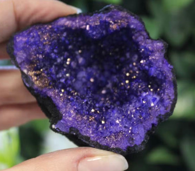 Dyed amethyst geode half held in hand showing vivid violet-purple crystal cluster detail up close