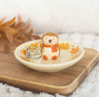 Hedgehog ceramic ring dish with rings on wooden board and autumn leaf backdrop