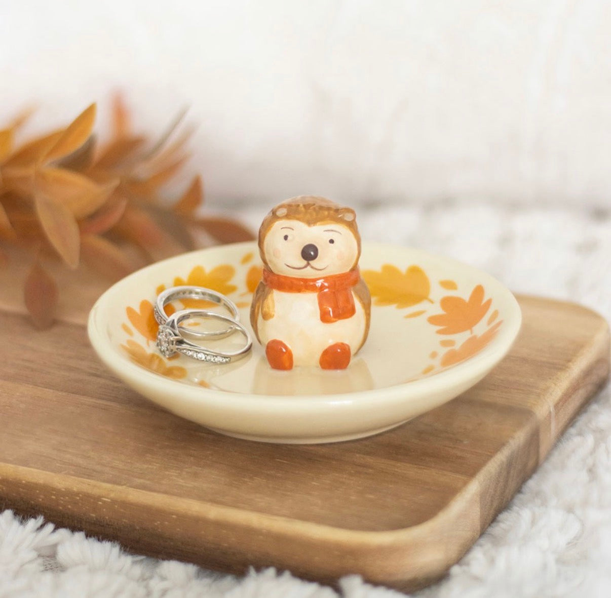 Hedgehog ceramic ring dish with rings on wooden board and autumn leaf backdrop