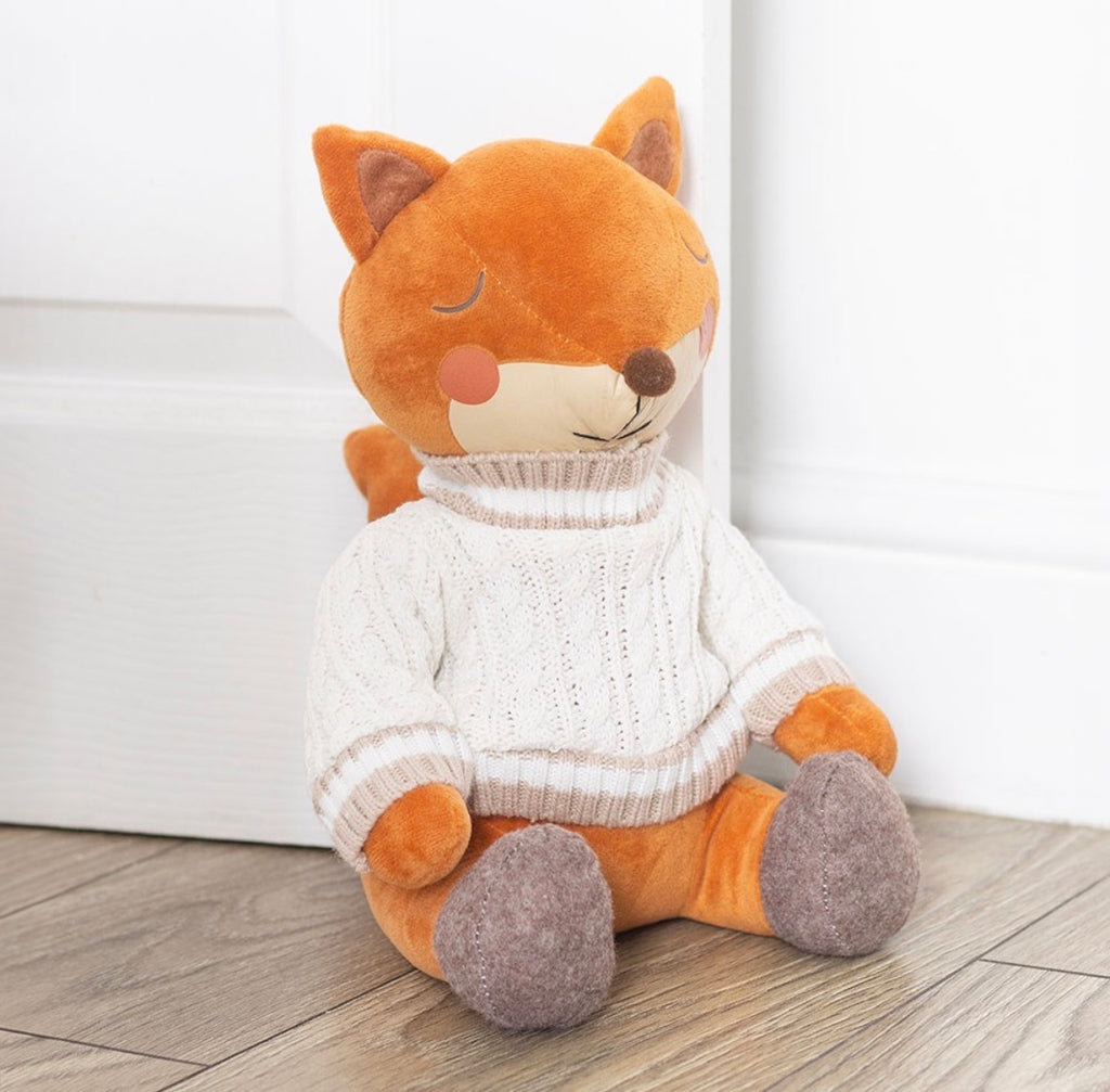 Flynn The Fox plush doorstop lifestyle shot propped against white door on wooden floor