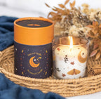 Spiced Vanilla celestial scented candle lit in glass jar beside navy gift box in lifestyle setting with dried flowers