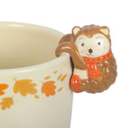 Close up of hedgehog figure on ceramic plant pot rim showing orange scarf and autumn leaf print detail