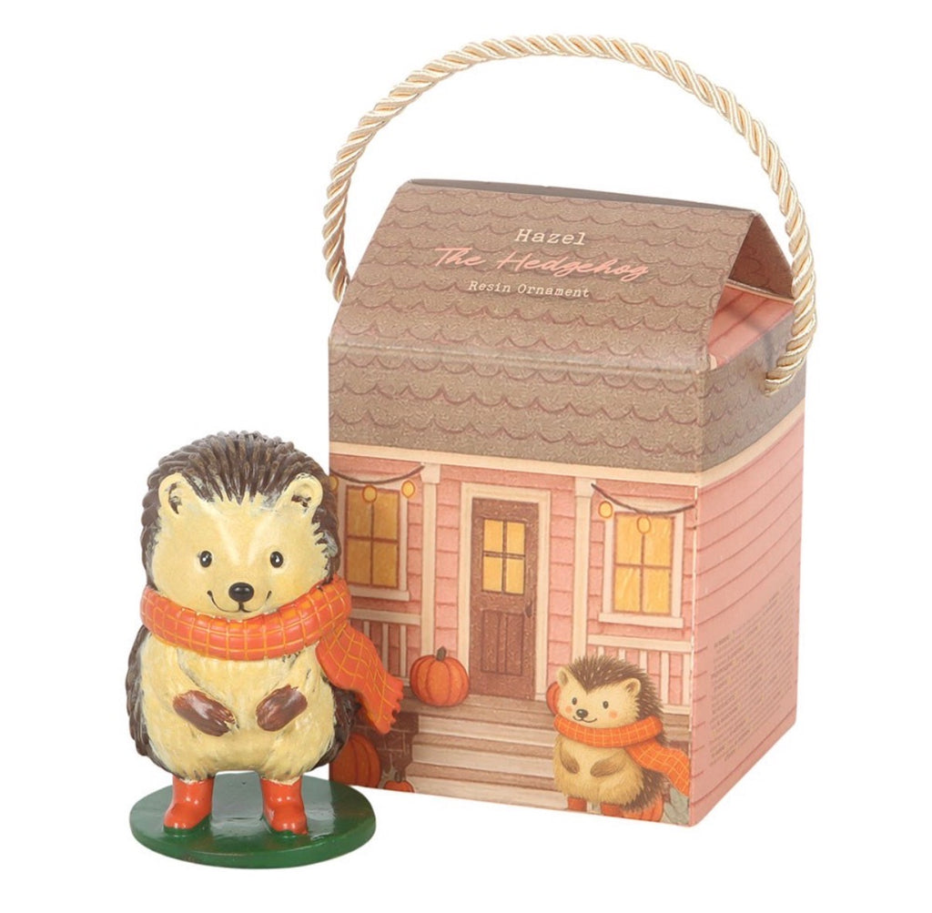 Hazel The Hedgehog resin ornament standing beside cottage house gift box on white background