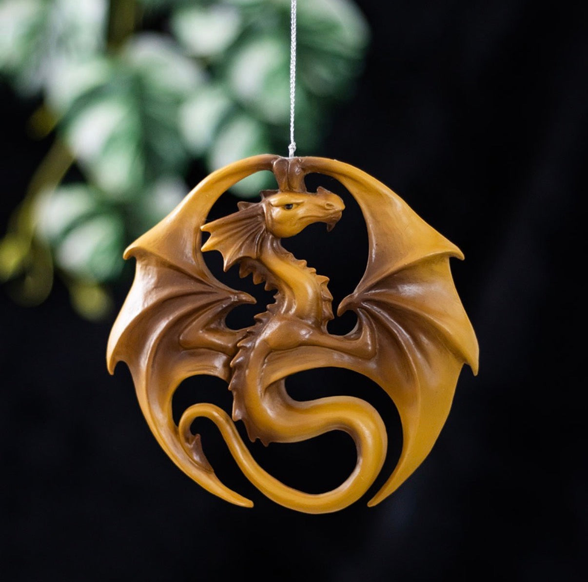 Anne Stokes golden dragon circular hanging ornament shown against a dark moody background with foliage