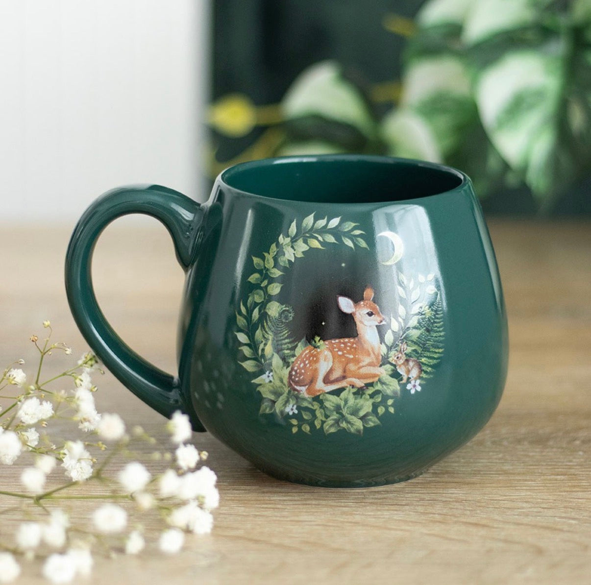 Enchanted Forest Fawn Mug in deep forest green with moonlit fawn and botanical wreath design, styled with baby's breath flowers