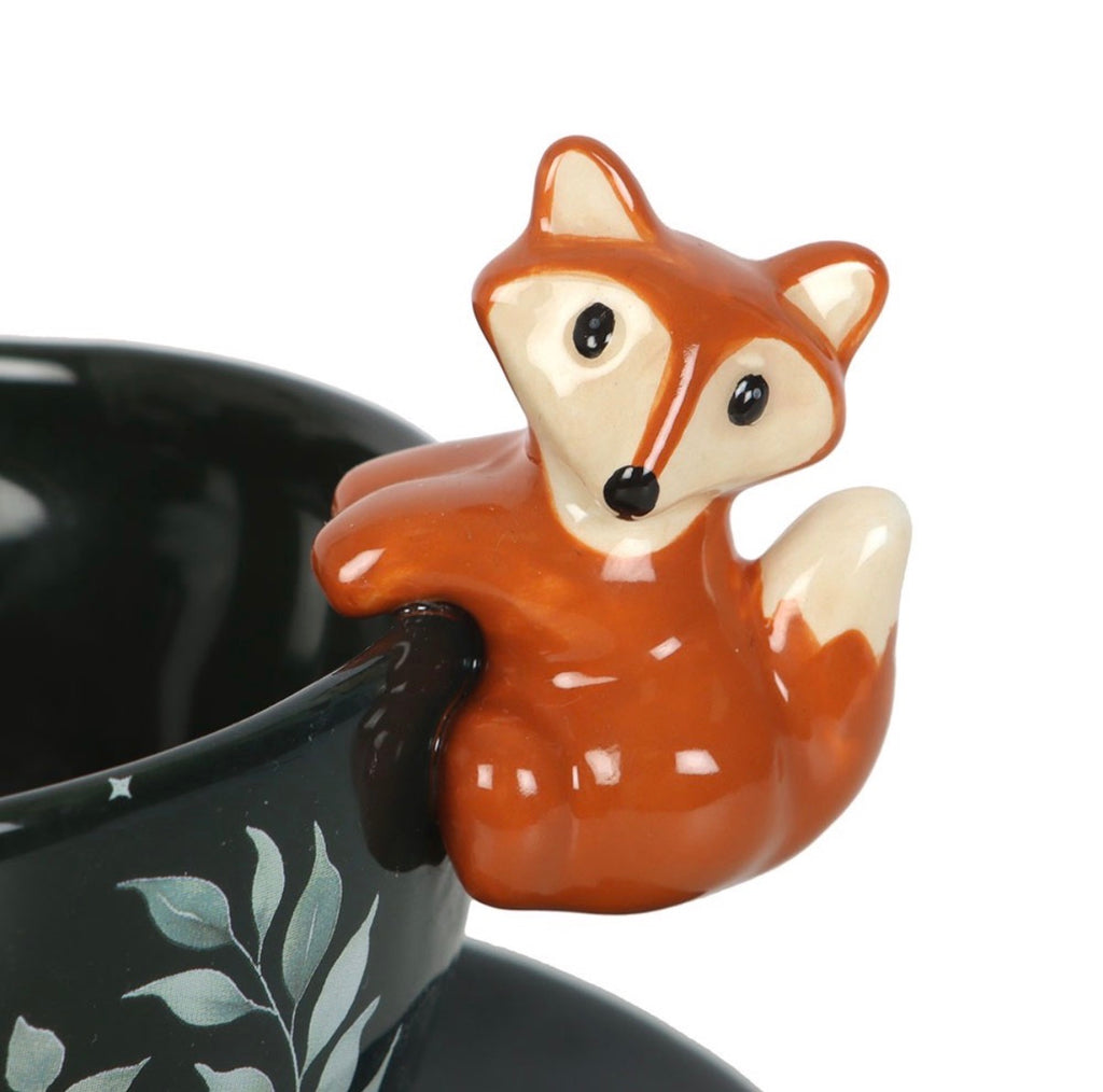 Close up detail of ceramic fox figurine perched on the rim of dark green enchanted forest tea cup