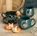 Enchanted forest fox tea cup alongside matching green ceramic mugs with woodland animal designs, styled flat lay