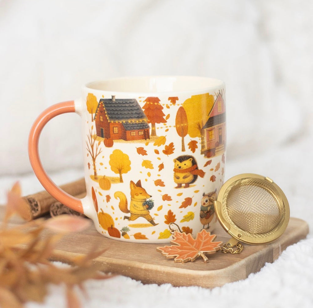 Creature Comforts autumn woodland mug with gold tea strainer and maple leaf charm, styled lifestyle shot on wooden board with cinnamon sticks