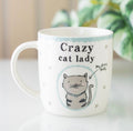 Crazy cat lady ceramic mug with sketched tabby cat illustration and My Furry Baby label, lifestyle shot with plant background