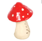 Small ceramic mushroom oil burner with cap on showing glossy red spotted cap and cream body, white background