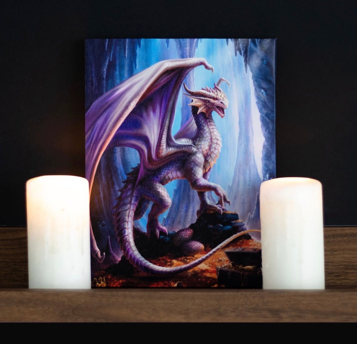 Anne Stokes Treasure Trove canvas print displayed on wooden shelf between two white pillar candles against dark background