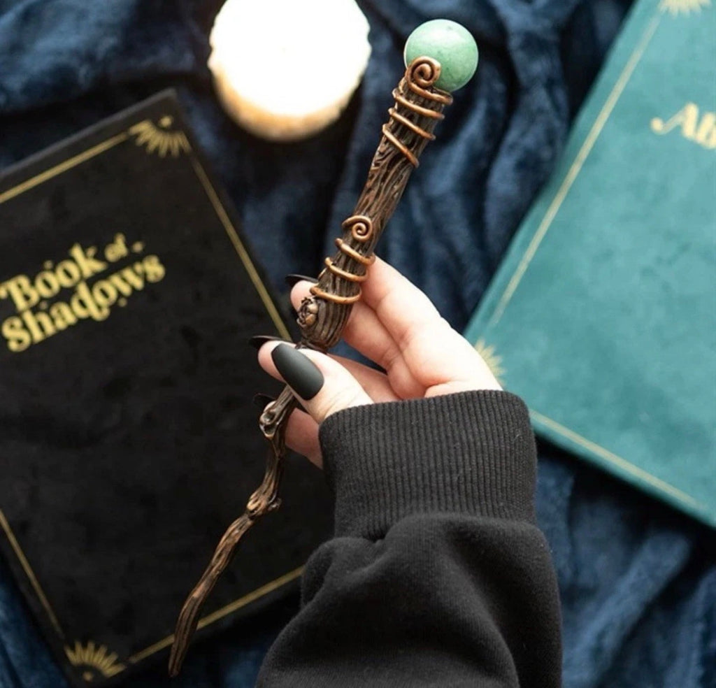 Hand holding Green Aventurine Abundance Wand with Book of Shadows in background